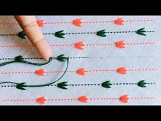 someone is stitching flowers on a piece of fabric with green thread and orange needles