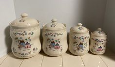 three ceramic canisters with houses and flowers painted on them, sitting on a tile floor