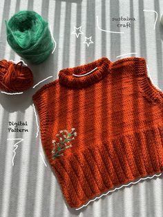 an orange knitted sweater next to balls of yarn