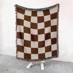 a woman standing in front of a brown and white checkered blanket with fringes