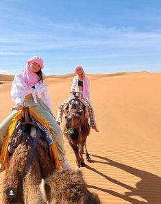 two girls are riding camels in the desert