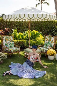 a woman sitting on the grass in front of some lawn chairs and an open umbrella