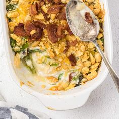 a casserole dish with bacon, cheese and spinach in it next to a spoon