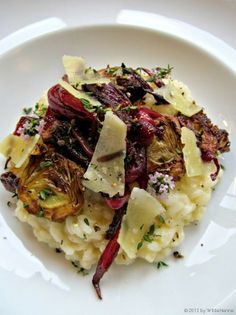 a white plate topped with pasta and artichokes on top of a table