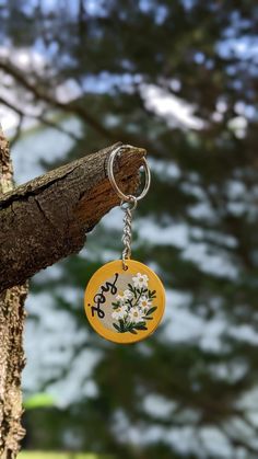 a yellow keychain hanging from a tree with flowers on it's side