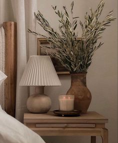 a table with a lamp and vase on it next to a bed in a room