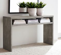 a console table with books and plants on it in front of a large framed mirror