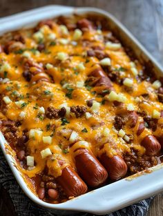 a casserole dish filled with chili, cheese and hotdogs on a wooden table