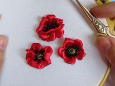 someone is working on some red flowers with gold trimmings and scissors to make them look like they have been made out of fabric