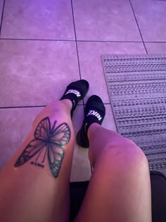 a woman's legs with a butterfly tattoo on her left leg and black shoes