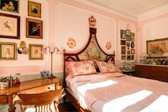 a bedroom with pink walls and pictures on the wall above the bed, along with an antique desk