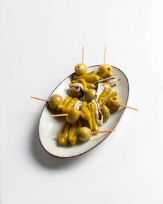 several skewered olives on a white plate with toothpicks in them