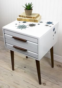 a white table with two drawers and a potted plant sitting on top of it