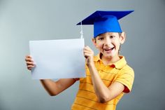 a young boy wearing a graduation cap and holding up a white paper with a blue tassel on it