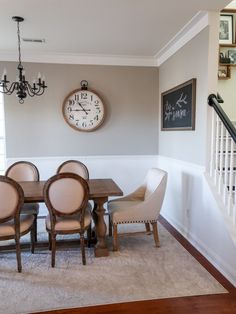 a dining room table and chairs with a clock on the wall above it in front of stairs