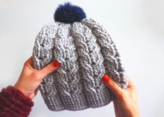 a woman holding up a knitted hat with a blue pom - pom