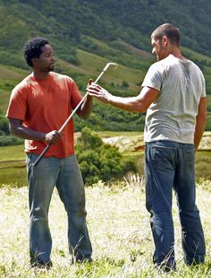 two men are standing in the grass and one is holding a stick with his hand