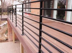 a wooden deck with black iron railings next to a brick wall and building in the background