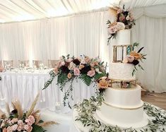 a wedding cake with flowers and greenery on the top is surrounded by white linens