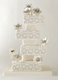 a wedding cake with white flowers on top is decorated in silver and white laces