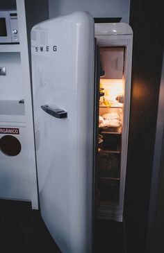 an open refrigerator with the door ajar in front of it, next to a microwave oven