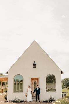 a bride and groom standing in front of a small white church with the doors open