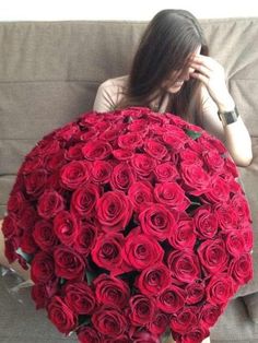 a woman sitting on a couch holding a large bouquet of red roses