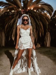 a woman standing in front of a palm tree wearing sunglasses and a white dress with lace on it