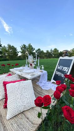 a table set up with red roses in the foreground and a chalkboard sign on it