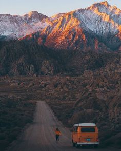 an orange van parked on the side of a dirt road in front of snow capped mountains