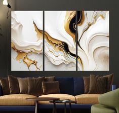 three abstract paintings in gold and white on a wall above a couch with a coffee table