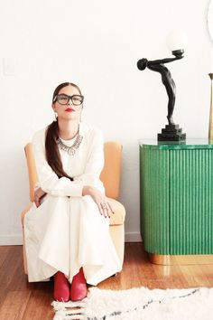 a woman sitting on a chair in front of a green cabinet with a statue behind her