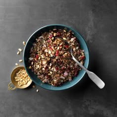 a bowl filled with granola and nuts next to a spoon on top of a table