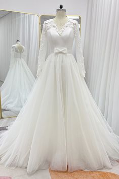 a white wedding dress with long sleeves and a bow on the waist is displayed in front of a mirror