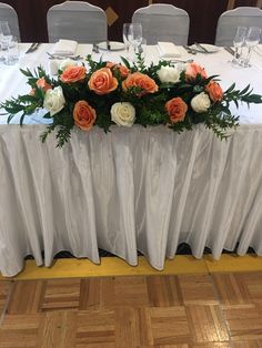 the table is set with white linens and orange flowers on it, along with silver chairs