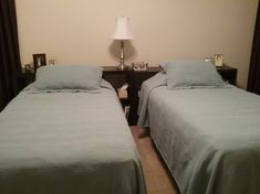 two twin beds in a hotel room with blue sheets and pillows on them, next to a night stand