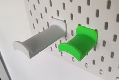 there is a green plastic object on the wall next to a white pegboard that has holes in it