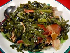 a white plate topped with greens covered in bacon and other toppings next to a spoon