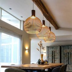 three lights hanging from the ceiling above a table with chairs and vases on it