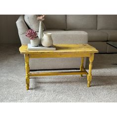 a yellow coffee table sitting in front of a couch with a vase on top of it