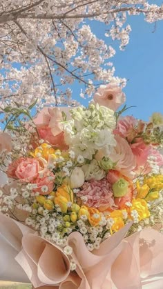 a person holding a bouquet of flowers under a tree with blue sky in the background