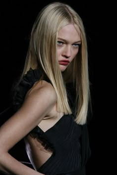 a woman with long blonde hair and blue eyes is looking at the camera while standing in front of a black background