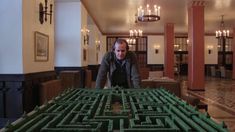 a man standing in front of a large green maze on the floor with chandeliers