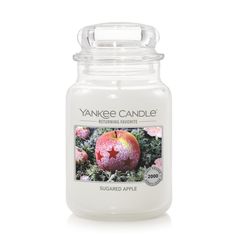 yankee candle with an apple on the front and bottom, surrounded by pink flowers in the background