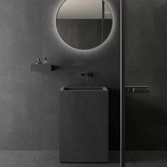 a bathroom with a round mirror above the sink and a black tiled wall next to it