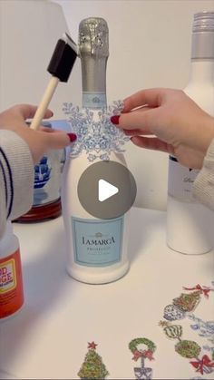 two hands are painting a bottle with snowflakes on it and another hand is holding a brush