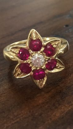 a gold ring with red stones and a white diamond in the center on a wooden surface