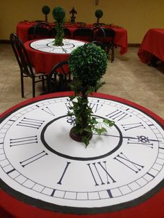 a table topped with a large clock face covered in greenery and surrounded by red tables cloths