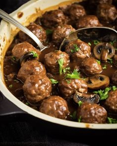 meatballs and mushrooms are being cooked in a skillet with a ladle on the side