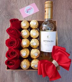 a bottle of wine and some chocolates in a box with red roses on the table